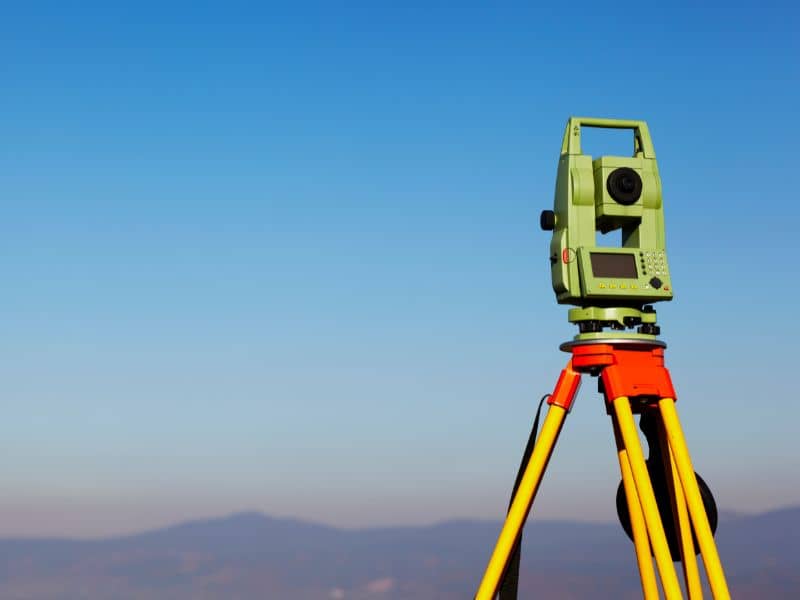 Dahne Land Surveying - Surveying total station on a yellow tripod against a clear blue sky, set up for field measurement.